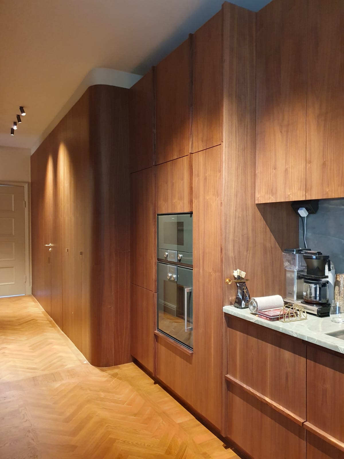 Tall walnut kitchen cabinets with integrated ovens and a curved corner