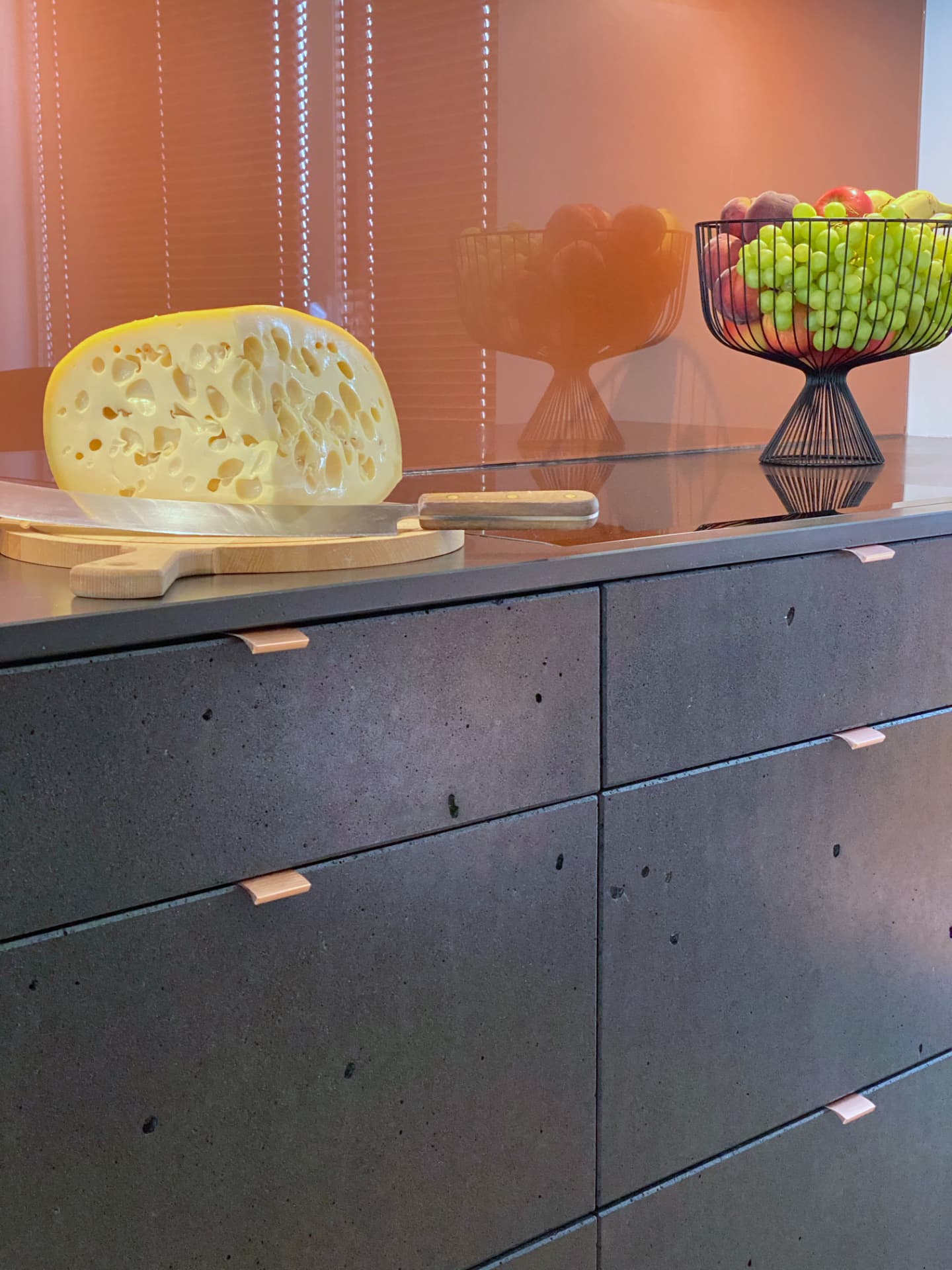 Concrete-effect kitchen drawers with wooden handles and a terracotta glass wall