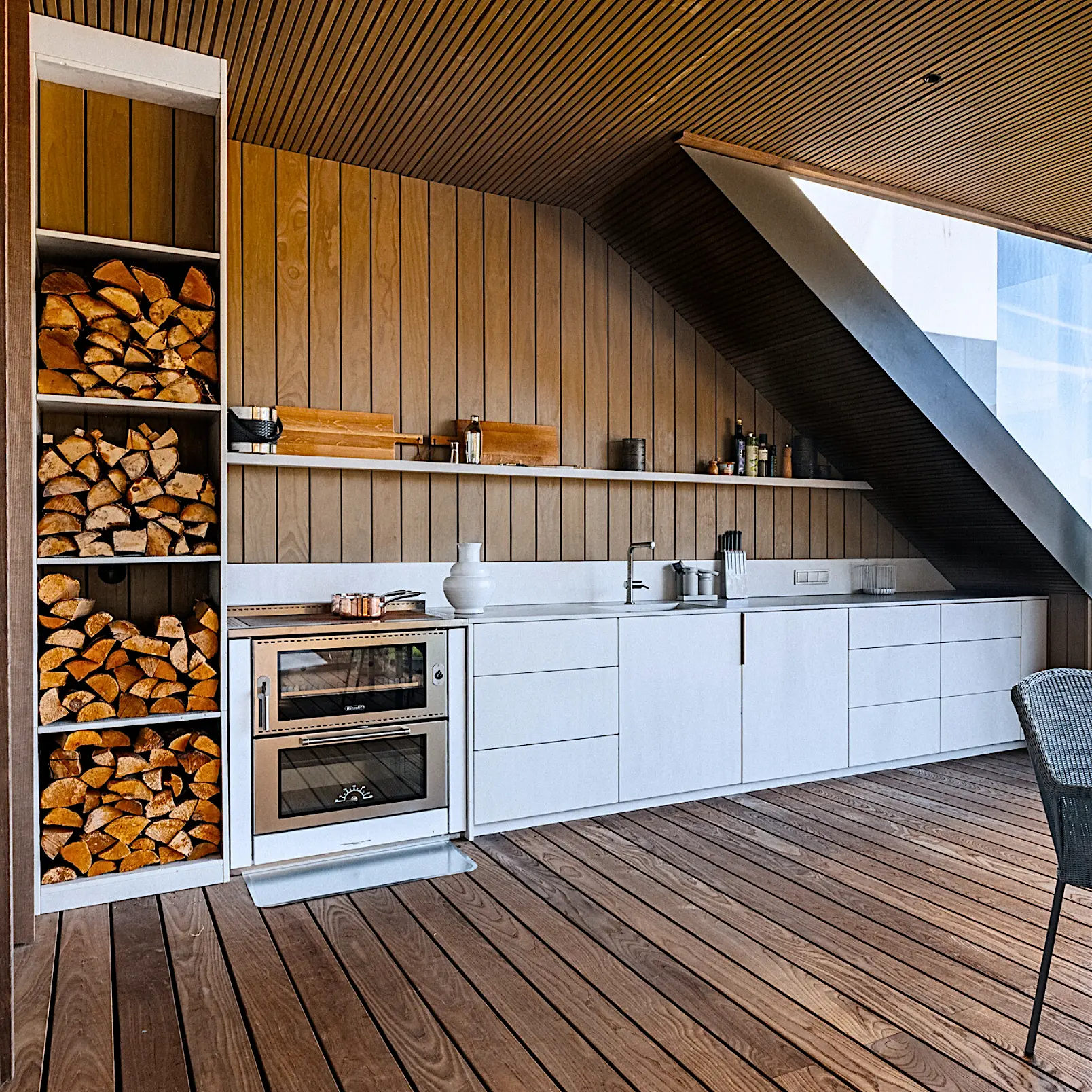 White kitchen with a wooden ceiling on the terrace next to a firewood store
