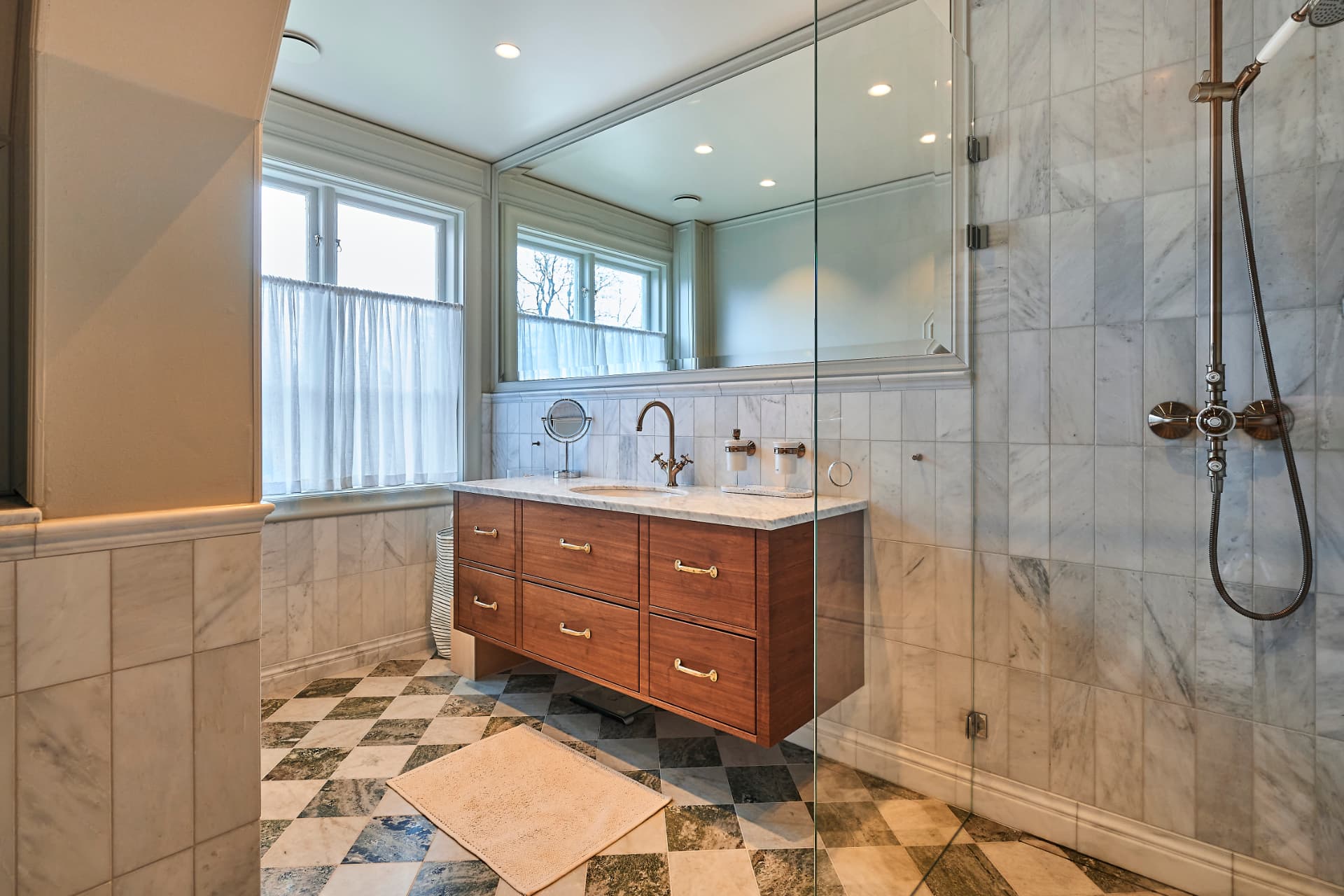 Bright bathroom with a wooden drawer vanity unit, a glass shower wall and patterned flooring