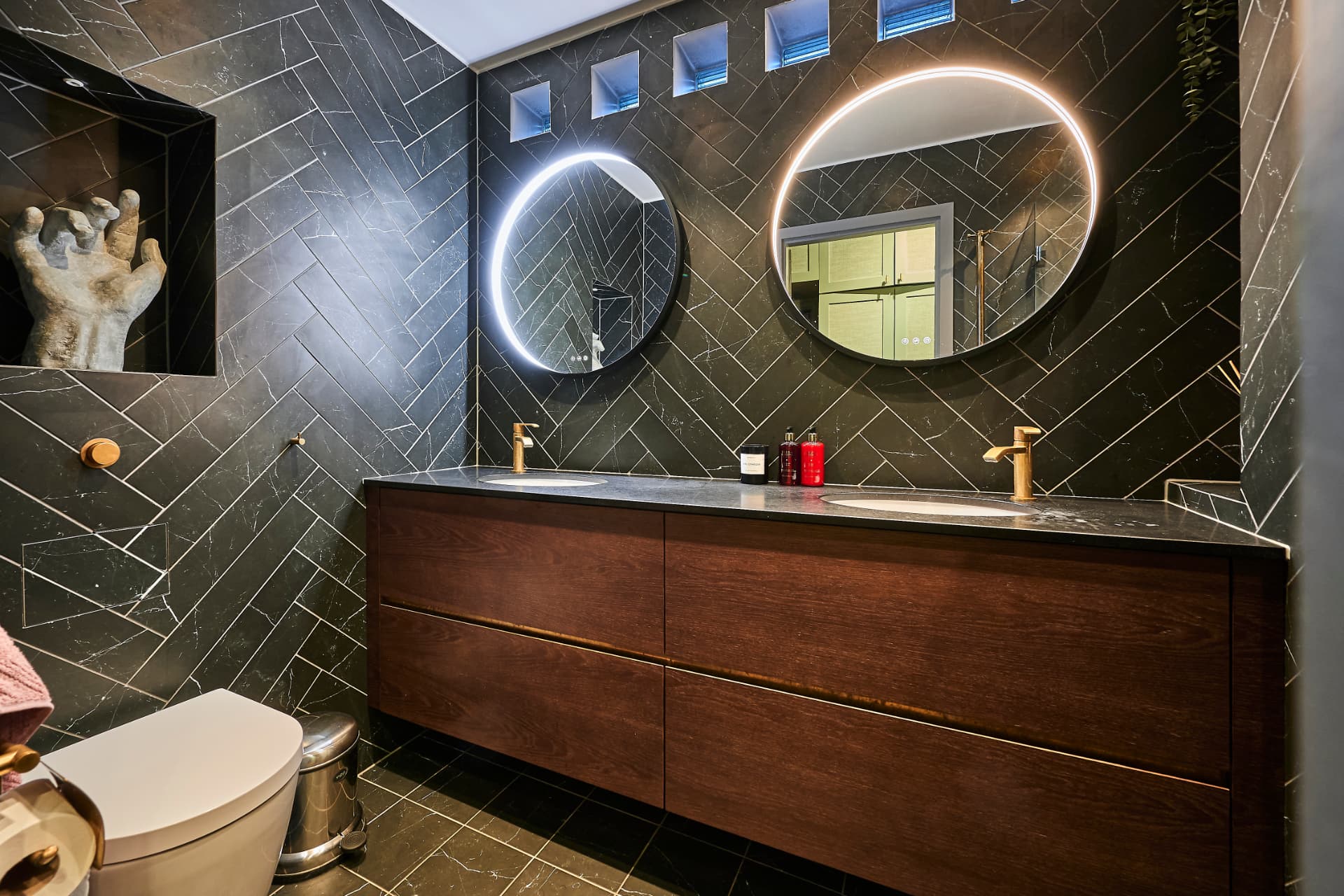 Dark bathroom with patterned tiles, a walnut vanity unit and illuminated mirrors