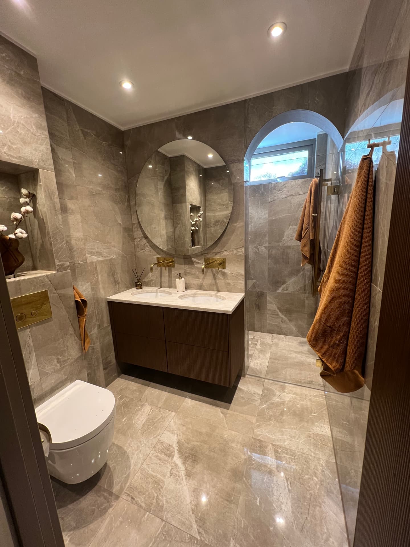 Grey bathroom with a dark vanity unit and an arched mirror