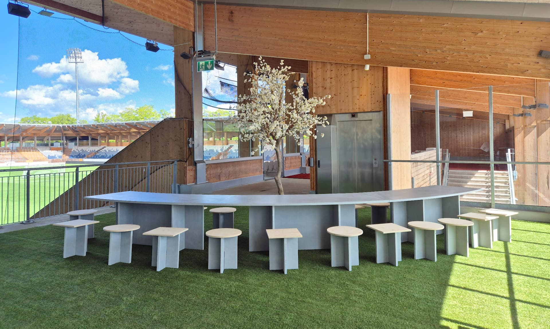 Böjd betongbänk och sittplatser i ett övertäckt utrymme intill en stadion